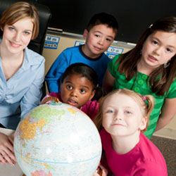 A teacher sits in a classroom with elementary school students.